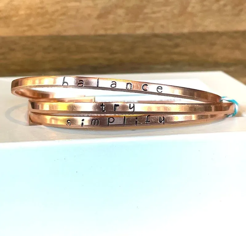 Hand-stamped copper bracelet trio that reads Simplify & Try & Smile